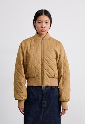 Chaqueta bomber acolchada en tono beige con cierre de cremallera, cuello y puños acanalados. Combinada con una falda de mezclilla oscura. Textura suave y diseño acolchado.