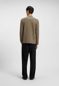 Top a maniche lunghe verde oliva realizzato in tessuto liscio, abbinato a pantaloni neri dalla vestibilità ampia. Design semplice senza motivi o dettagli evidenti.