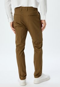 Brune skræddersyede bukser med slim fit, der har to baglommer og en glat tekstur, parret med hvide sneakers.