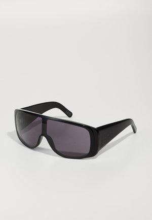 Lunettes de soleil noires avec un grand design enveloppant, verres teintés sombres et monture en plastique robuste. Présente un logo sur la branche.