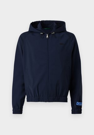 Jachetă navy cu glugă ajustabilă, închidere cu fermoar în față, manșete elastice și talie cu șnur. Dispune de un logo mic pe piept.
