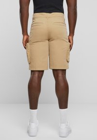 Shorts cargo beiges avec poches latérales, présentant une coupe droite et un tissu doux. Associés à des baskets blanches et des chaussettes montantes.