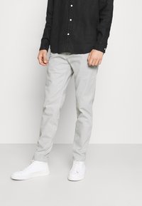 Lichtgrijze chino's van katoen, met een rechte pijp. Gecombineerd met witte hoge sneakers en een zwart shirt met lange mouwen.