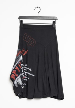 Jupe asymétrique noire avec texte imprimé rouge et blanc, graphique papillon, et sections plissées suspendue sur un cintre noir.