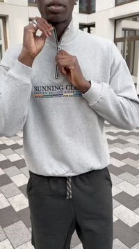 Felpa grigia chiara con zip a mezzo e testo "RUNNING CLUB" in blu navy e strisce colorate, abbinata a joggers neri con coulisse.