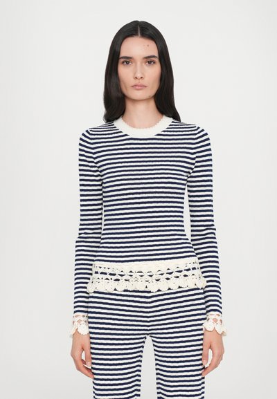 Maglione a righe bianche e blu navy con maniche lunghe, scollatura a onda e bordo in pizzo all'orlo e ai polsini. Texture a costine in tutto il capo.