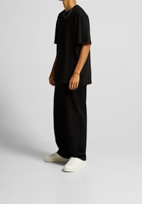 Camiseta negra oversized de mangas cortas, combinada con pantalones holgados negros y zapatillas blancas, creando un look casual monocromático.