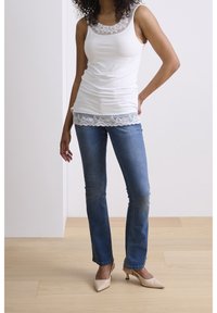 Top blanco sin mangas con encaje en el escote y el dobladillo, combinado con jeans ajustados de mezclilla azul y zapatos de tacón nude.