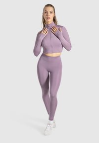Lilla atletisk sæt består af en cropped zip-up jakke og højhyggede leggings. Materialet er glat med en tætsiddende pasform og lange ærmer.