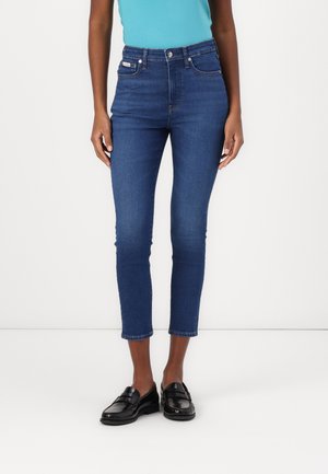 High-waisted, dark blue denim jeans with a slim fit, cropped length, and five pockets. Smooth texture with subtle stitching details.