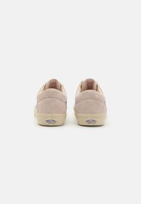 Une paire de baskets Vans en daim rose clair vues de l'arrière avec des semelles beiges et des logos "Off The Wall" sur les onglets des talons.