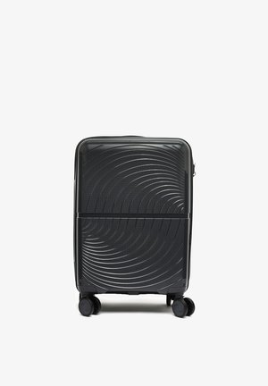 Valise rigide noire avec des motifs texturés circulaires, quatre roues pivotantes et une ligne de séparation horizontale au milieu.