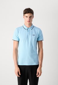 Polo en coton de couleur bleu clair avec un col à bord noir et blanc, deux boutons et un petit logo noir sur la poitrine.