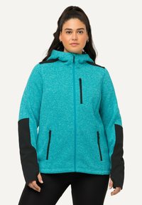 Giacca teal con zip, realizzata in tessuto testurizzato, con accenti neri sulle spalle e sui polsini, dotata di tasche con zip sui lati e sul petto.