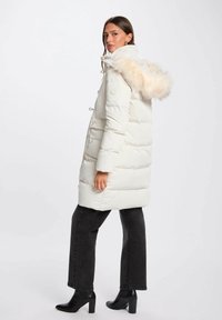 Parka bianca gonfiabile con cappuccio in pelliccia sintetica, polsini a coste e coulisse regolabili. Indossata sopra jeans neri e stivali con tacco.