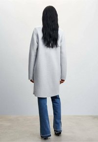 Lichtgrijze lange jas met een gestructureerde afwerking, gecombineerd met flare denim jeans. De jas heeft een rechte snit en lange mouwen.