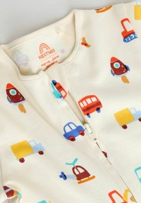 Bavlnený spací overal so zipsovým zapínaním, krémový podklad s farebnými vzormi vozidiel, vrátane rakiet, áut a nákladných áut. Mäkká textúra.