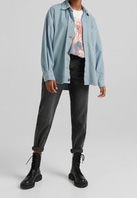 Camicia di velluto a coste blu chiaro, t-shirt bianca con grafica, jeans neri a gamba affusolata e stivali da combattimento neri con lacci e suole spesse.