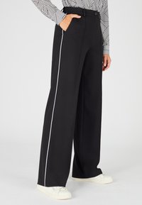 Zwarte wijde broek met witte zijstrepen, met een gladde textuur en zakdetails, gecombineerd met witte sneakers.
