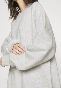 Sudadera de gran tamaño en gris claro con mangas largas y relajadas, y puños acanalados. Textura suave y diseño simple, sin patrones ni detalles visibles.