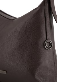Bruine leren schoudertas met een gestructureerd oppervlak, gebogen vorm en een metalen ringaccent. Heeft een enkele strap om te dragen.