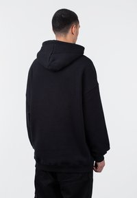 Felpa nera con cappuccio realizzata in tessuto misto cotone; presenta una vestibilità rilassata, polsini a costine e spalle scese per comfort e facilità.
