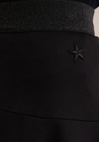 Falda de tela negra con una cintura elástica negra brillante que presenta un detalle de bordado en forma de estrella en el lateral. Textura suave en general.