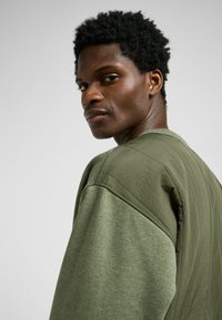 Olijf groene oversized sweatshirt met textuur mouwen, ronde hals en zichtbare naden. Gemaakt van zachte, lichte stof.