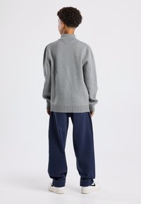 Light gray pullover sweater with a high collar, made from textured material. Paired with loose-fitting navy blue pants and white sneakers.