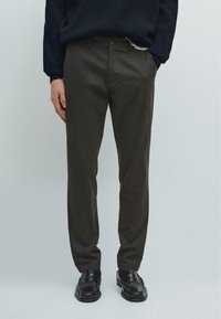 Mørkebrune tapered bukser lavet af letvægtsstof, med flad front, bæltestropper og sidelommer, parret med sorte sko.