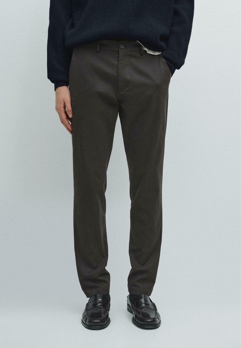 Mørkebrune tapered bukser lavet af letvægtsstof, med flad front, bæltestropper og sidelommer, parret med sorte sko.