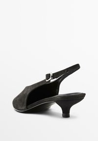 Svart mocka slingback-sko med låg klack, som har en justerbar rem och en böjd silhuett. Slät inre foder och subtil glans.