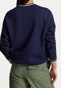 Marinblå sweatshirt med ribbade ärmslut och krage, prydd med vita ränder; kombinerad med olivgröna cargobyxor med bakfickor.