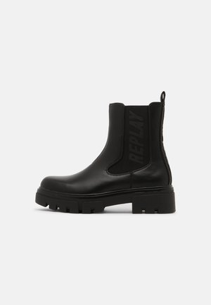 Bottine noire en cuir avec semelle épaisse, panneau latéral élastique, languette de tirage, et logo "REPLAY" sur le côté.