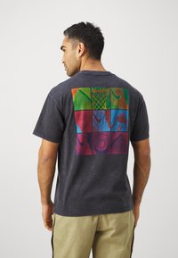 Short-sleeve, dark gray t-shirt with a multicolored graphic of nine square panels on the back, featuring various textures and patterns.