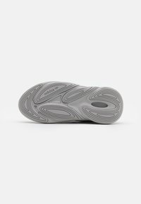 Harmaa tennaripohja, jossa on aaltoileva kuvio, tuntomerkit koostuvat teksturoiduista urista ja "adidas"-logosta lähellä kantapäätä. Litteä muotoilu, kumimateriaali.