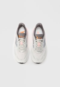 Une paire de chaussures de course New Balance blanches et grises avec un logo orange "TCS New York City Marathon", vues d’en haut sur un fond blanc.