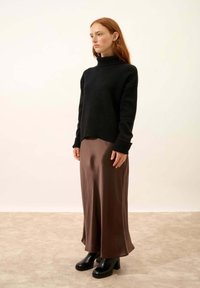 Czarny dziany sweter z wysokim kołnierzem, zestawiony z brązową satynową spódnicą na cienkich ramiączkach i czarnymi botkami na platformie, stojący na neutralnym tle.