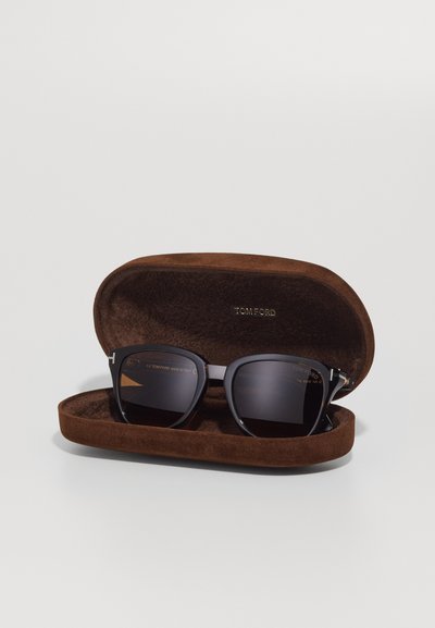 Black sunglasses with dark lenses, square frame, silver accents, housed in a brown suede case with embossed brand name.