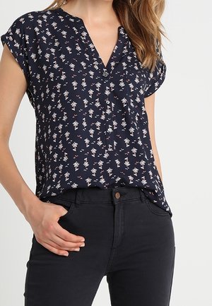 Marineblouse met korte mouwen, v-hals en kleine bloemenprint. Zachte stof, comfortabele pasvorm, licht gebogen zoom, gecombineerd met donkere broek.
