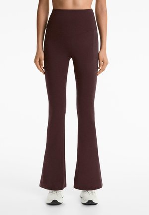 Burgunderfarbene, hochgeschnittene, ausgestellte Leggings mit glatter Textur und Nahtdetails, kombiniert mit weißen Sportschuhen.