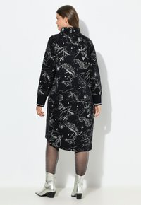 Schwarzes knielanges Kleid mit silbernen himmlischen Mustern, hohem Kragen, langen Ärmeln und gerippten Bündchen. Kombiniert mit glitzernden Strumpfhosen und silbernen Stiefeln.