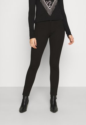 Leggings negros con un diseño ajustado, textura suave y tela elástica, combinados con una blusa negra adornada con un patrón geométrico brillante.