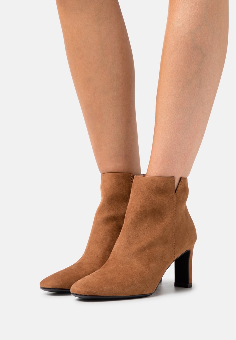 Braune Wildleder-Stiefeletten mit einer spitzen Zehenpartie, hoher Blockabsatz und einem kleinen Ausschnitt am oberen Rand. Ganze Fläche mit glatter Textur.