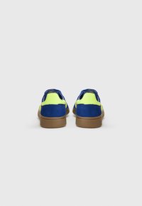Blå og neon gule sneakers med overdækning i ruskind, rund form, gummisål og en struktureret brun ydersål. Bagfra ses de kontrasterende farver.