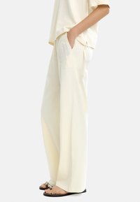 Jasno kremowe spodnie w luźnym kroju z bocznymi kieszeniami, wykonane z miękkiego materiału, z delikatnym haftem w kwiaty w pobliżu kieszeni. Noszone z płaskimi sandałami.