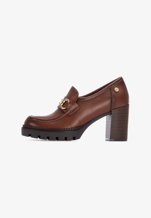 Moc shoes de cuero marrón con tacón, punta redondeada, hebilla decorativa, plataforma negra texturizada y tacón estriado. Acabado pulido.