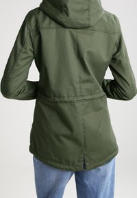 Veste à capuche vert olive en tissu résistant, dotée d'une taille cintrée, d'une fente au dos et de détails cousus. Design décontracté avec manches longues.