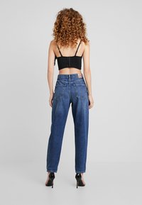 Tummansiniset korkeavyötäröiset rentomalliset farkut, joissa takataskut ja näkyvä merkkilappu oikean taskun yläpuolella.