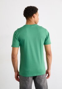 Grøn bomulds t-shirt, korte ærmer, rund hals, glat tekstur, tætsiddende design, bagview, parret med grå jeans.